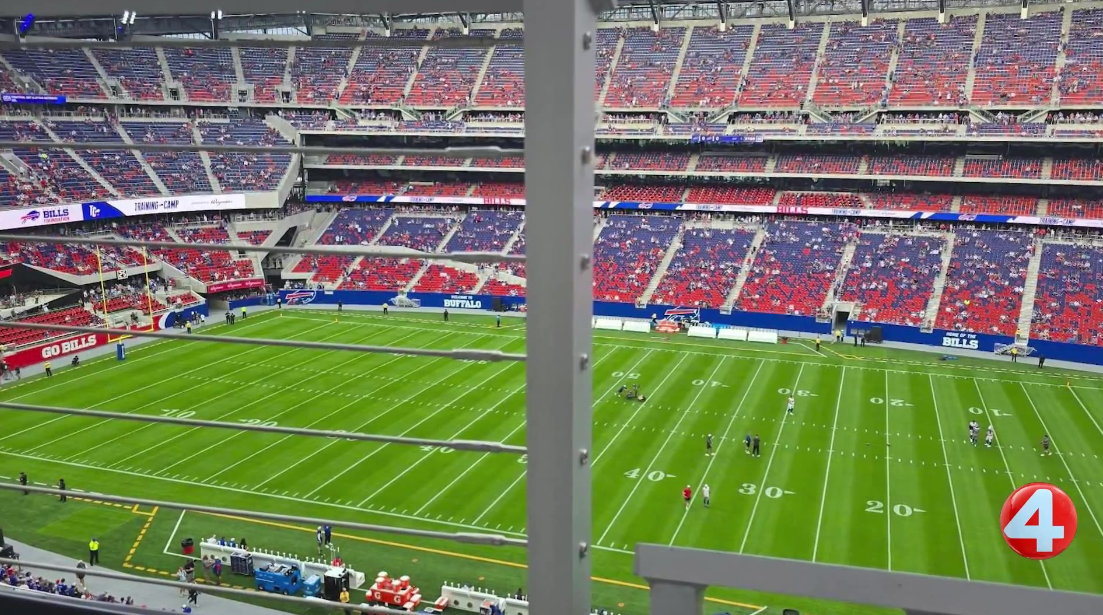 A metal railing and support pole cut directly across the field view from an upper-deck seat at Highmark Stadium, obscuring the far sideline. WIVB/News 4 Buffalo footage from the August 8, 2026 Blue & Red open practice.